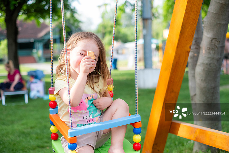 快乐的小女孩在户外儿童游乐场的秋千上玩耍图片素材