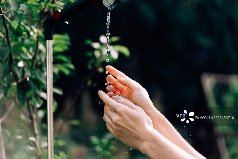 在自然环境中，手在户外水龙头下洗涤的特写镜头图片素材