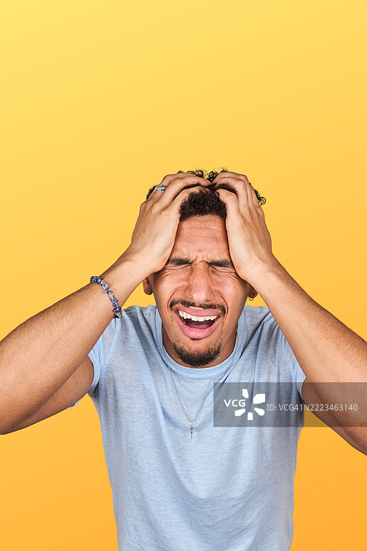 沮丧的年轻男子闭上眼睛，双手抱头以缓解压力图片素材