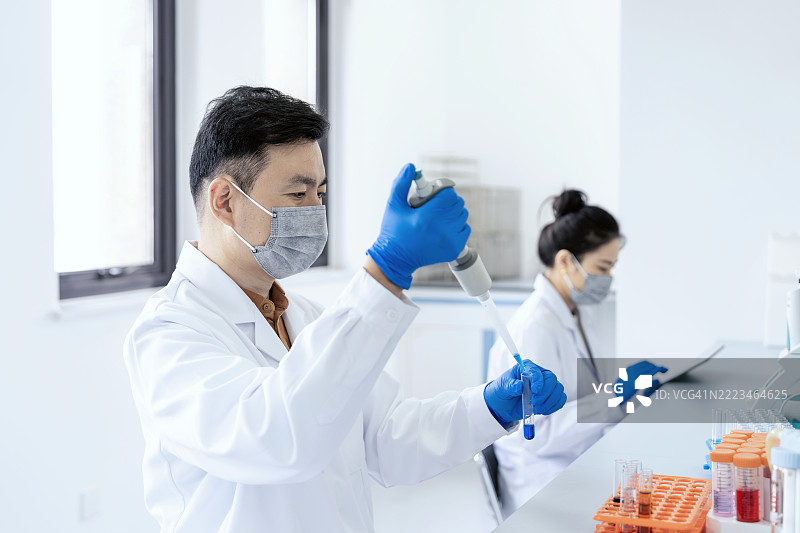 亚洲科学家在实验室中处理实验结果，手中拿着一个装有玻璃器皿的试管。科学实验室中的研究与开发概念。图片素材