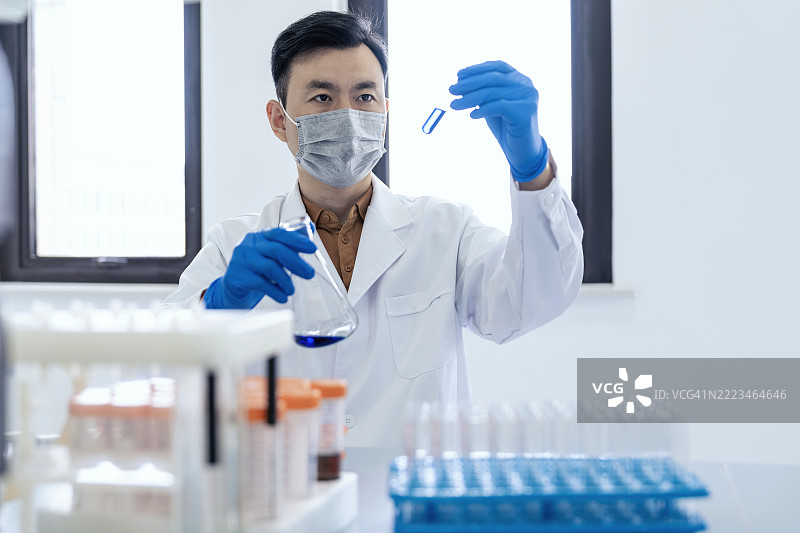 亚洲科学家在实验室中处理实验结果，手中拿着一个装有玻璃器皿的试管。科学实验室中的研究与开发概念。图片素材