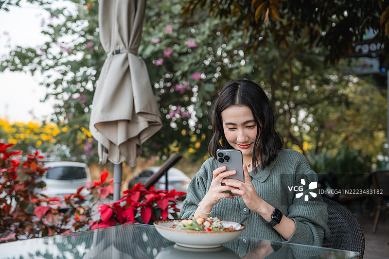 快乐的年轻女性在咖啡馆用智能手机拍摄她的食物图片素材