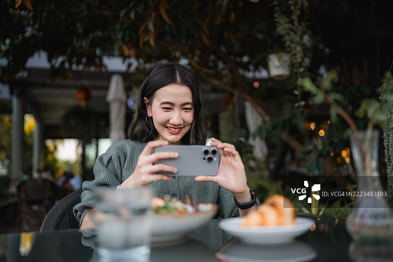快乐的年轻女性在咖啡馆用智能手机拍摄她的食物图片素材