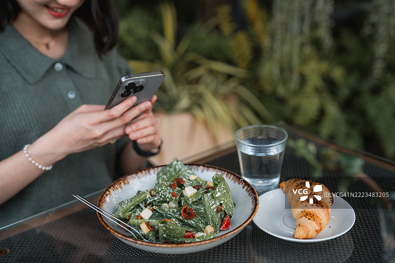 快乐的年轻女性在咖啡馆用智能手机拍摄她的食物图片素材