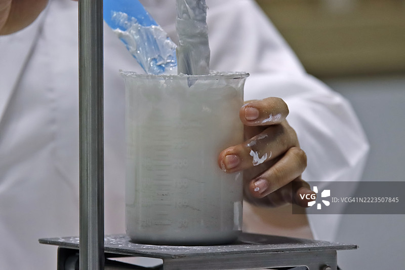 科学家的手在实验室的烧杯中搅拌粘稠的白色溶液。化妆品行业。图片素材