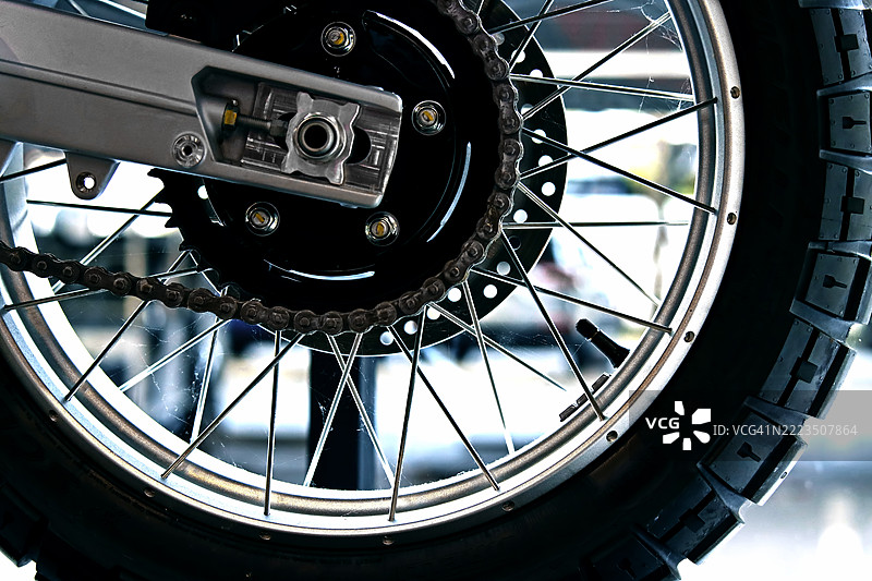 越野摩托车后部组件。特写镜头展示了带有坚固花纹轮胎和暴露链条驱动系统的辐条轮。图片素材