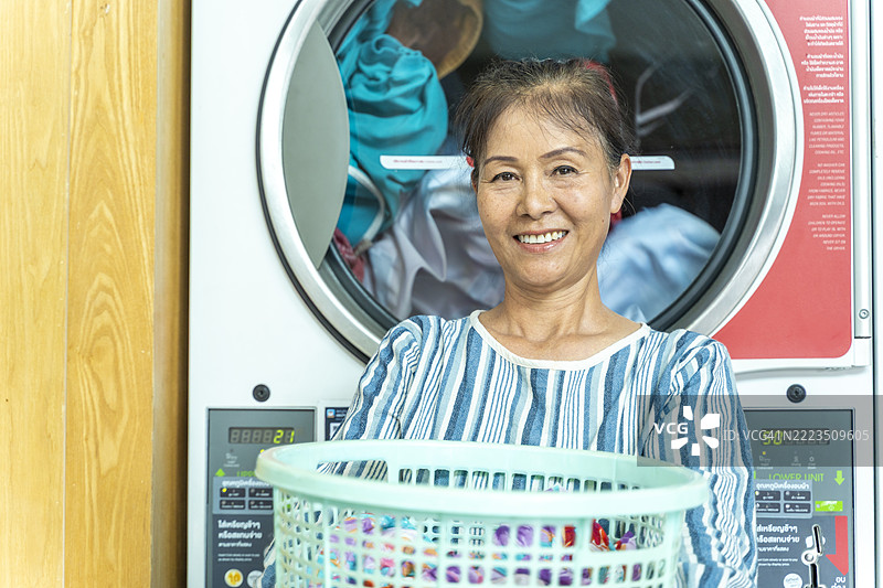 微笑的老年女性在自助洗衣店里抱着洗衣篮图片素材