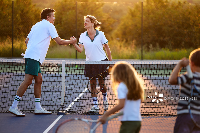 快乐的父母在球场上网球比赛后互相问候。图片素材