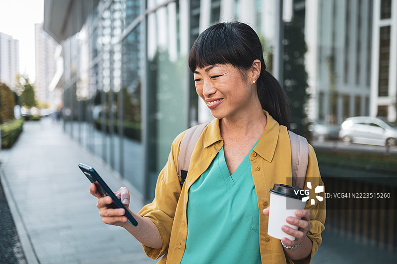 年轻女性在户外微笑着使用智能手机图片素材