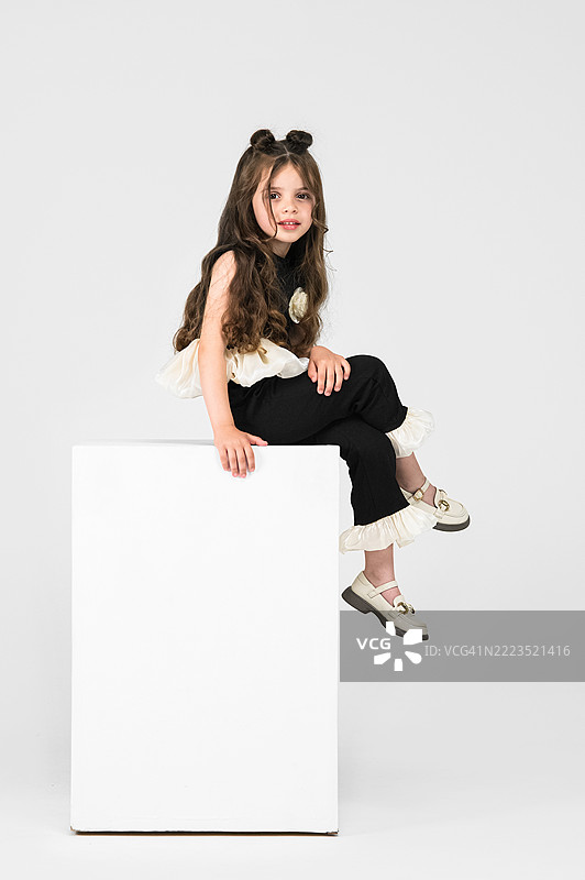 时尚的小女孩坐在工作室里的白色立方体上图片素材