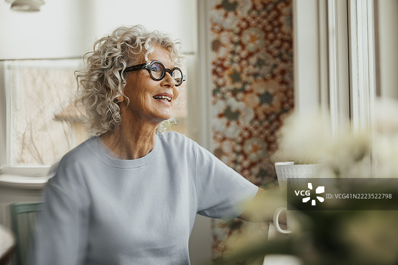 快乐的老年女性在家中透过窗户看外面图片素材
