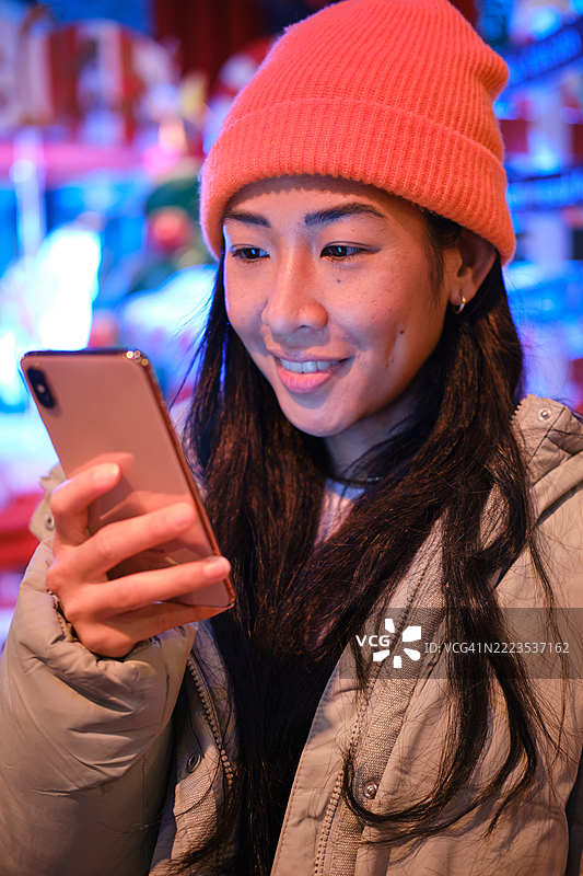 年轻亚洲女性在夜晚的圣诞装饰背景下使用智能手机图片素材