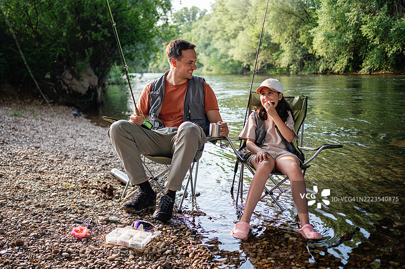父亲和女儿在宁静的河边一起享受钓鱼时光图片素材