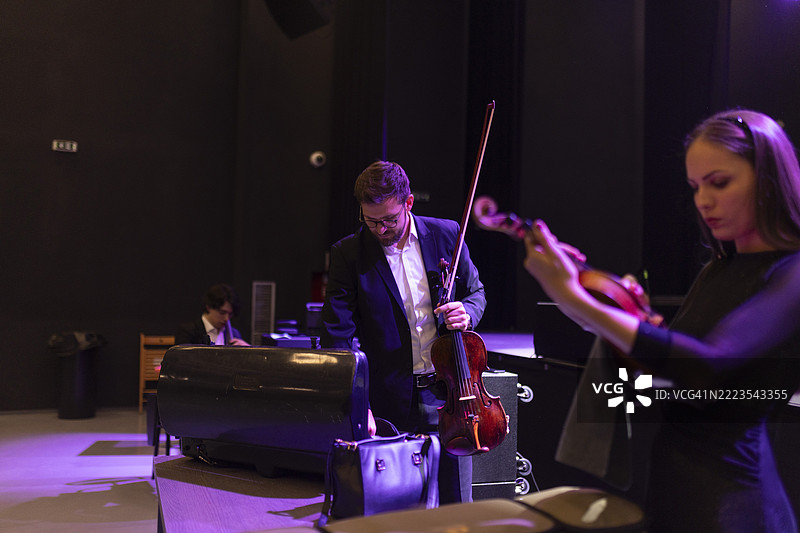 古典音乐会前的准备。一位女小提琴手在清洁她的乐器，而一位男艺术家正在从琴盒中取出中提琴。图片素材