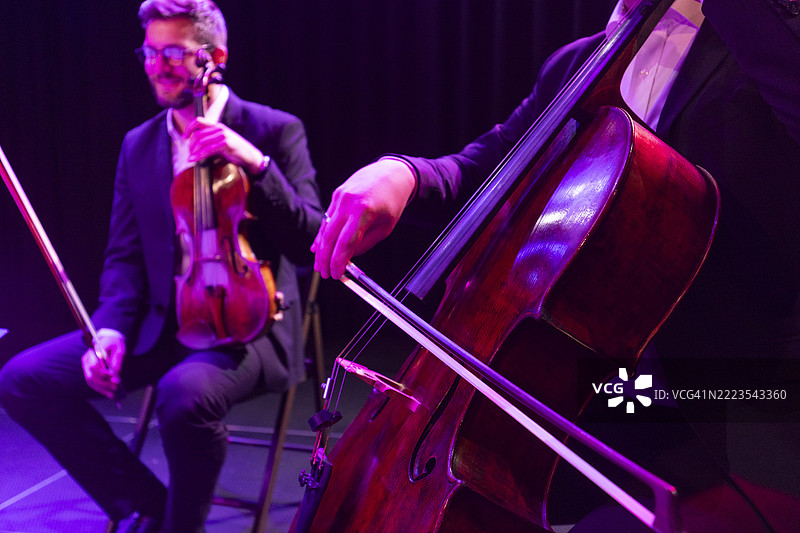 小提琴手和大提琴手在音乐会的舞台上并肩而坐，面向观众演奏古典音乐。图片素材