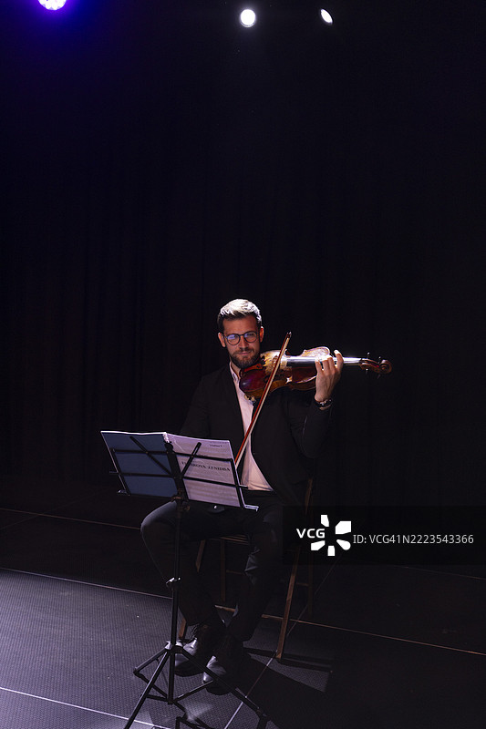 一位男音乐家优雅地演奏着中提琴。他的表情流露出激情与专注，突显了音乐艺术和个人表达。图片素材