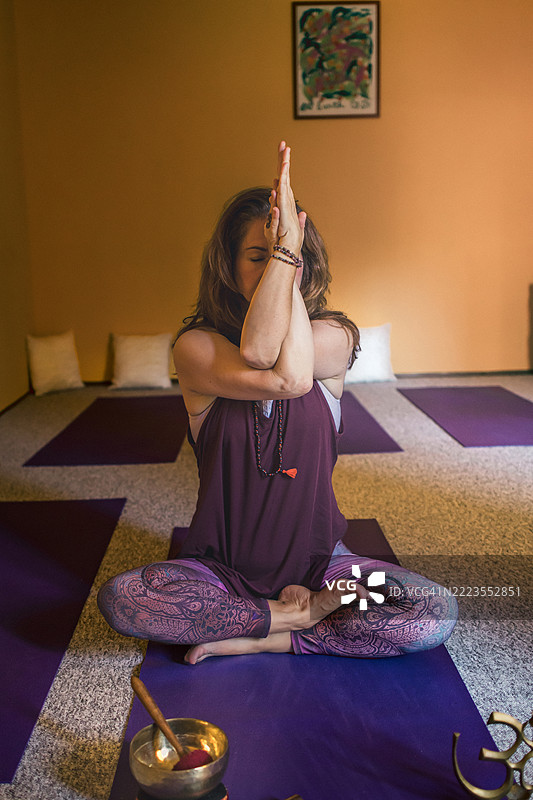 成熟女性瑜伽教练在瑜伽工作室的地板上冥想，使用治愈的西藏唱碗。冥想、减压、放松、心理健康、精神修炼。能量力量的概念。图片素材