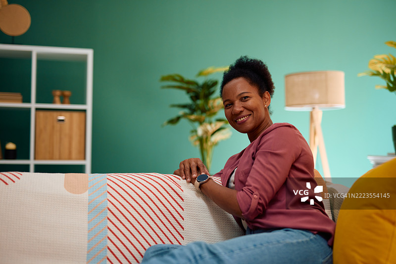 快乐的非裔美国女性在家中沙发上放松，面向镜头。图片素材