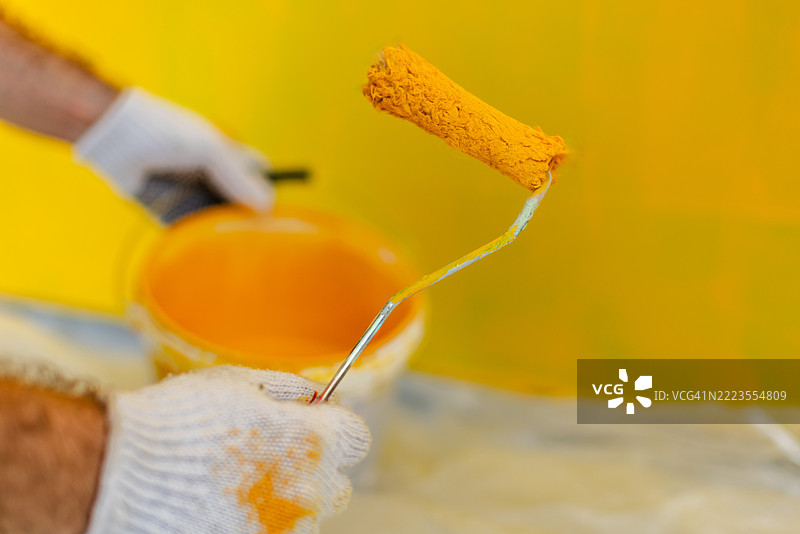 房屋油漆工戴着保护手套，用滚筒在室内墙壁上涂抹鲜艳的黄色油漆图片素材