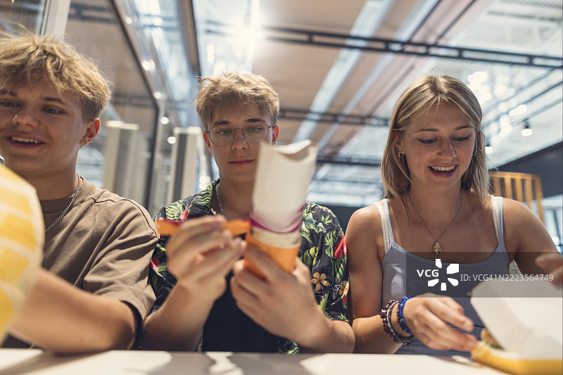 三个青少年朋友在现代城市美食广场享受休闲快餐午餐图片素材