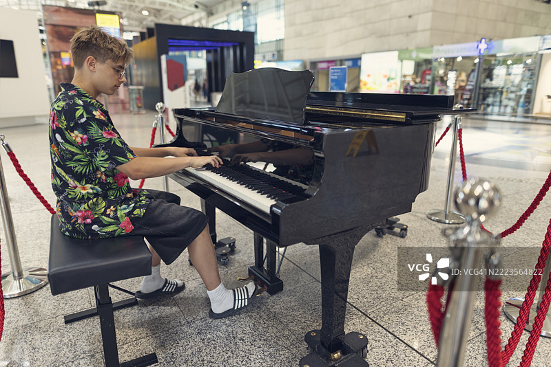 青少年音乐家在现代机场候机区的公共钢琴上表演。图片素材