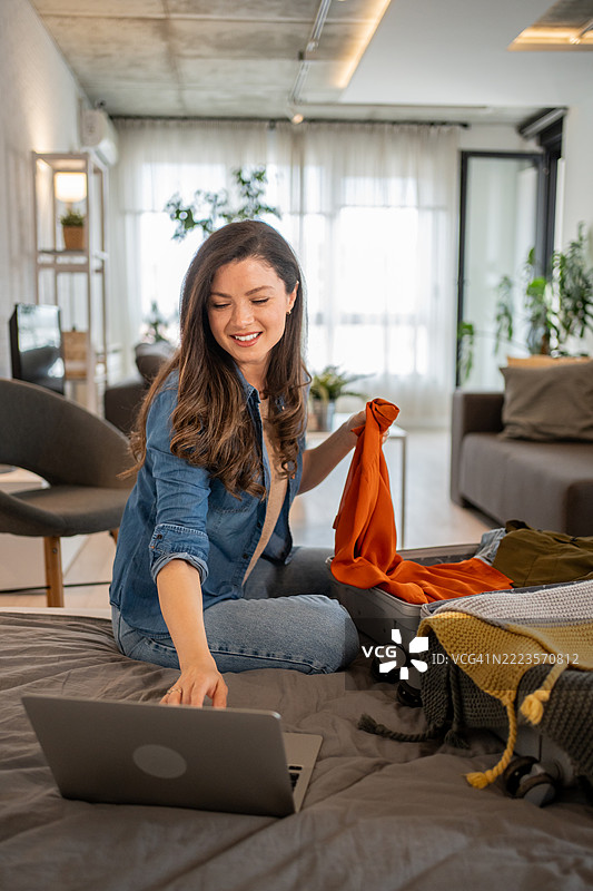 女人在打包行李箱，同时在笔记本电脑上浏览旅行网站图片素材