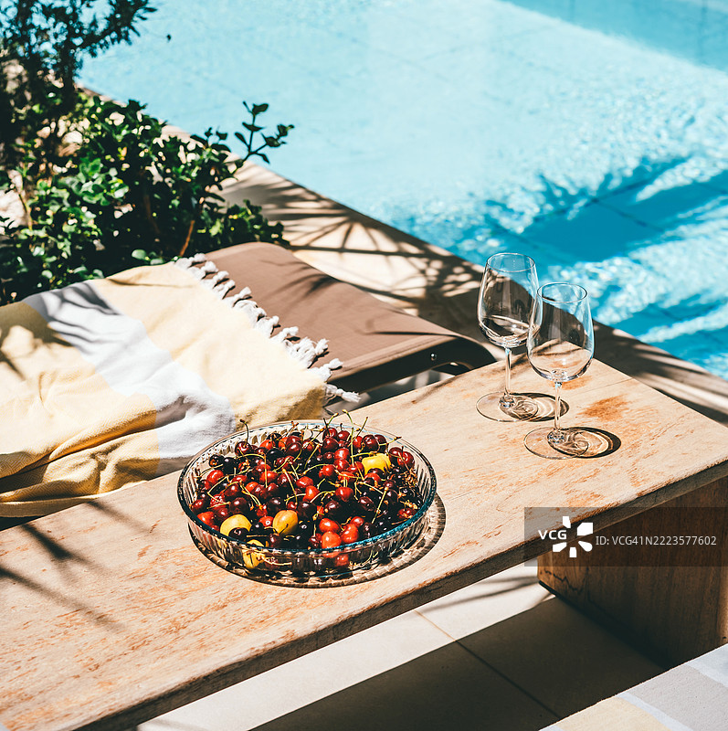 夏季泳池边的场景，摆放着樱桃、酒杯和阳光下的休闲布置图片素材