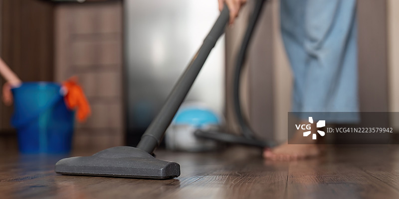 年轻女性赤脚在厨房地板上吸尘，专注于清洁图片素材