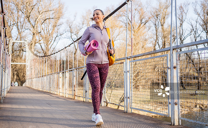 运动女性在桥上走，背着瑜伽垫和背包图片素材