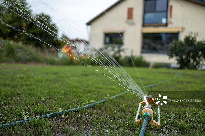 花园喷洒器在阳光明媚的日子里向郁郁葱葱的草坪喷洒水分，提供必要的水分补给。图片素材