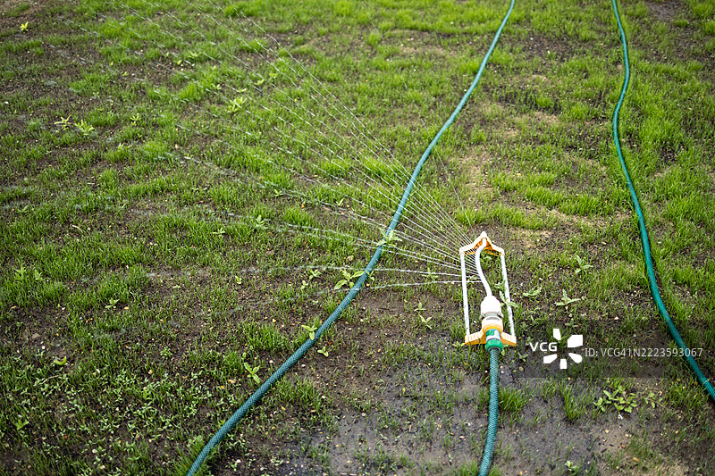 花园喷洒器在阳光明媚的日子里向郁郁葱葱的草坪喷洒水分，提供必要的水分补给。图片素材