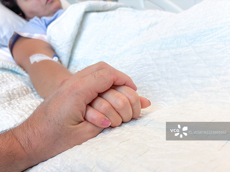 特写镜头：一名男子握着女性病人在医院病床上的手图片素材