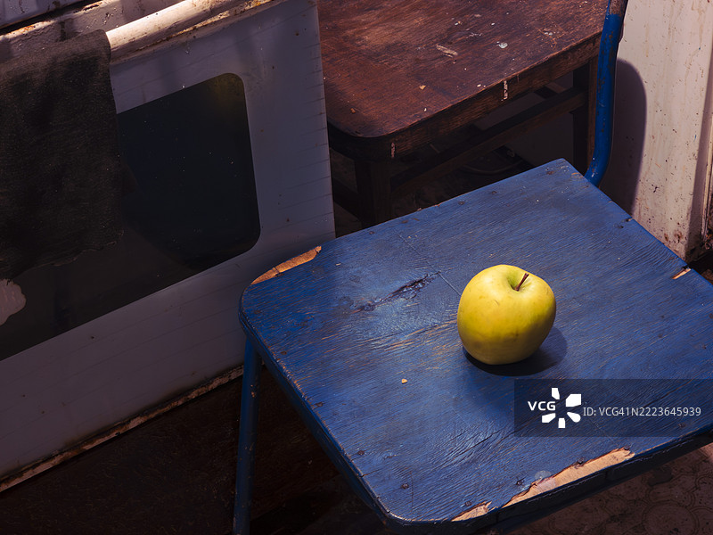 明亮的黄色苹果静静地放在一个古朴的蓝色凳子上，周围是温馨的灯光厨房环境，伴随着自然质感和黄昏时分的怀旧气息。图片素材