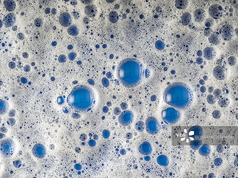 蓝色表面上的肥皂泡沫全景。图片素材