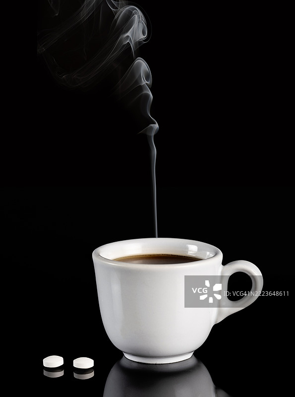 一杯冒着热气的咖啡和两片阿司匹林药片，背景为黑色。图片素材