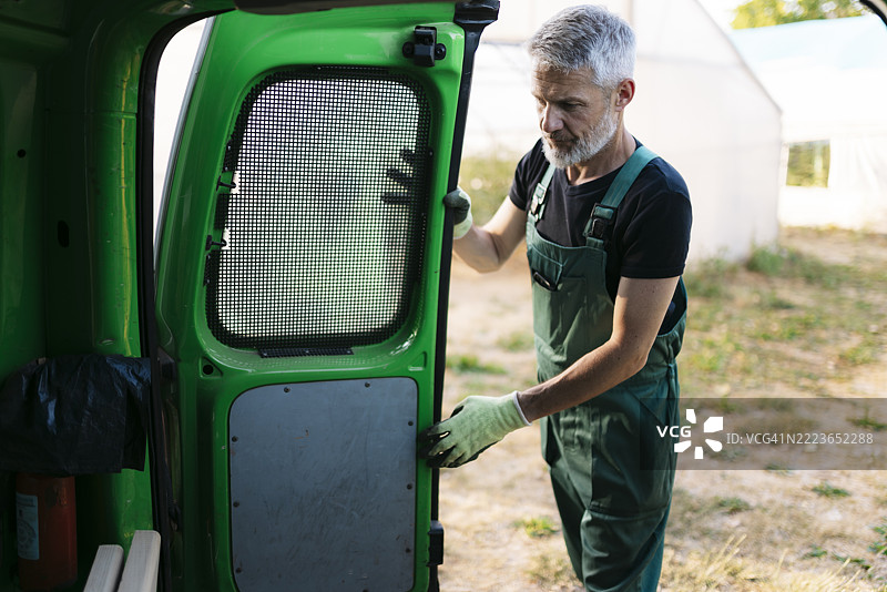 农民在温室附近关上他的绿色货车的门图片素材