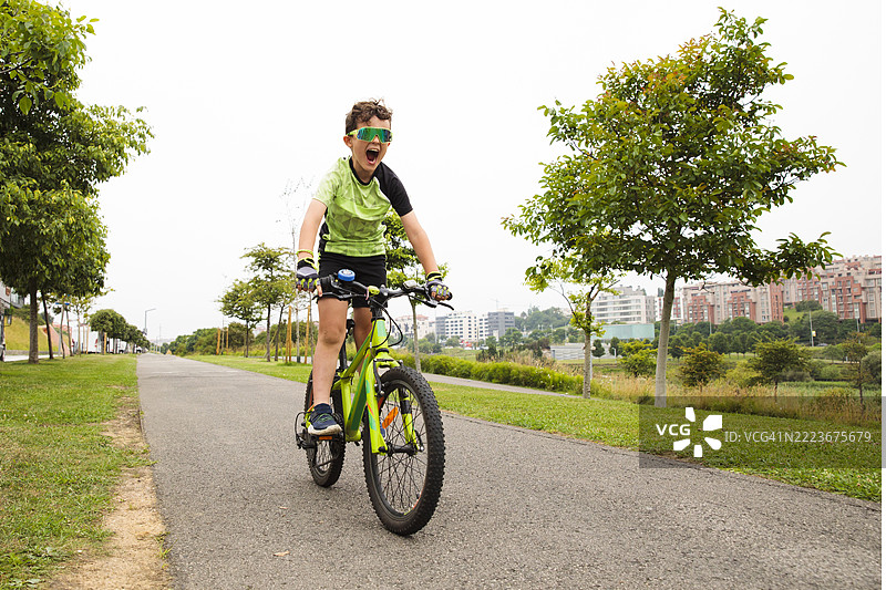 兴奋的男孩在公园里骑着自行车大喊图片素材