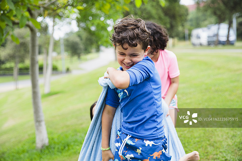 快乐的孩子们在公园里拉着裹在毯子里的朋友玩耍。图片素材