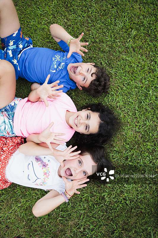 在公园里开玩笑和搞笑的孩子们躺着，对着镜头做鬼脸图片素材