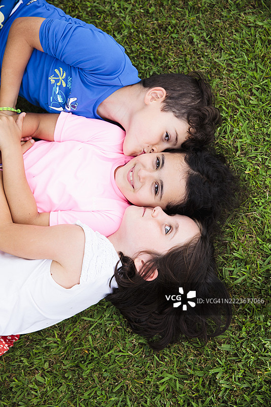 三个亲密的孩子在公园的草地上微笑着看向镜头图片素材