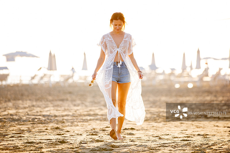 穿着长蕾丝裙的女人在日落时分赤脚享受沙滩漫步图片素材