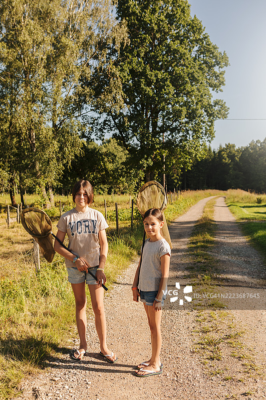 两个孩子在夏天的乡村里，各自拿着一个捕蝴蝶网。图片素材
