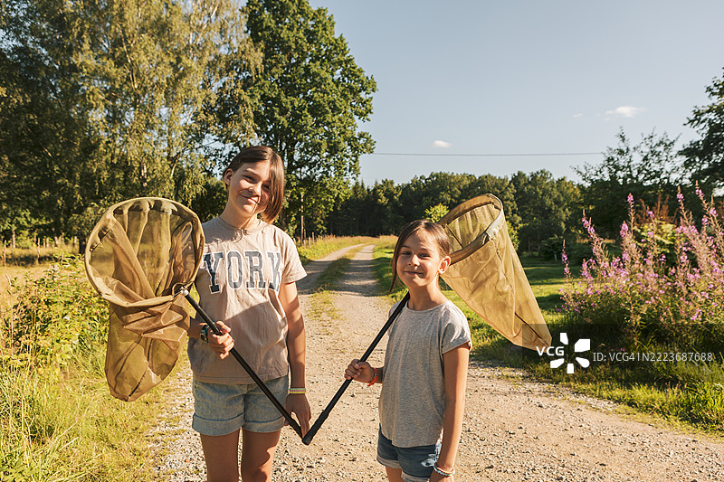 两个孩子在夏天的乡村里，各自拿着一个捕蝴蝶的网。图片素材