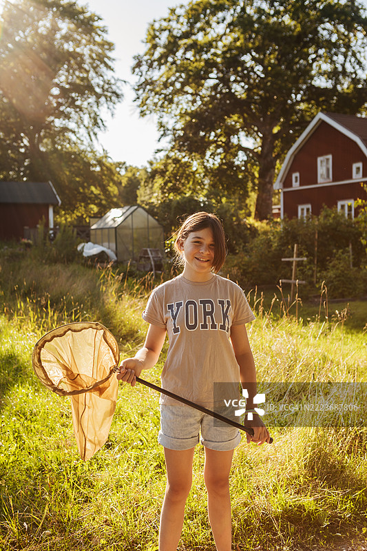 在夏季别墅中，逆光下的女孩与蝴蝶网的肖像。图片素材