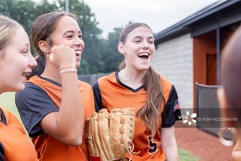 高中女子垒球运动员在靠近休息区的场边聚在一起欢笑图片素材