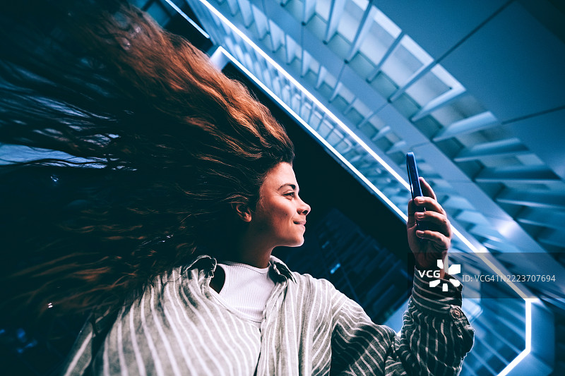 自信的女性在未来城市的霓虹空间中使用智能手机上的人工智能图片素材