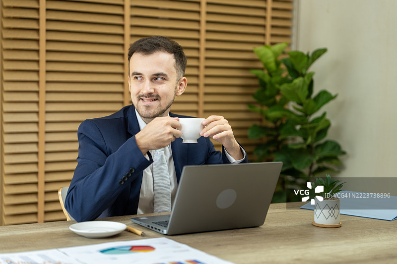商人在办公室里一边喝咖啡一边使用笔记本电脑工作图片素材
