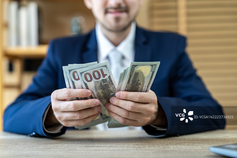 商人在办公室桌子上数一百美元的钞票图片素材