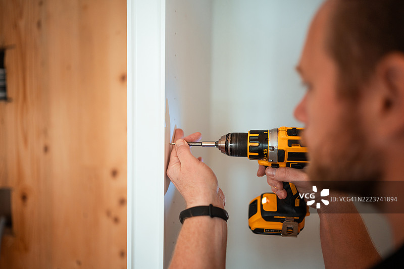 白人男性使用电钻进行厨房组装图片素材