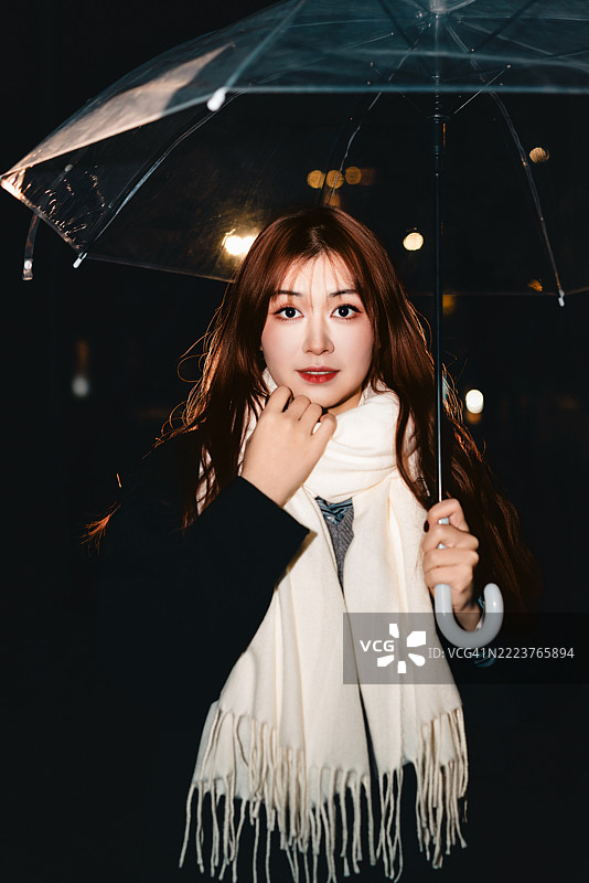 年轻女性在户外享受冬夜，轻轻抚摸着她的围巾。图片素材